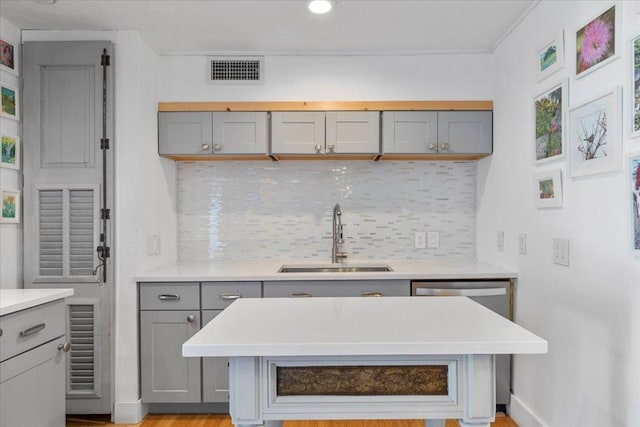 kitchen with a sink, gray cabinetry, light countertops, dishwasher, and backsplash