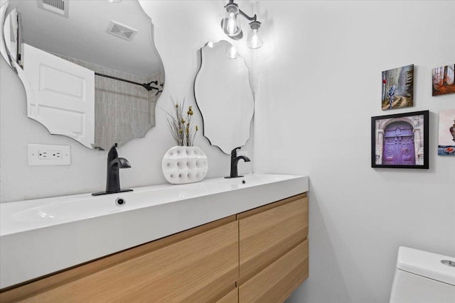 bathroom with double vanity, toilet, visible vents, and a sink