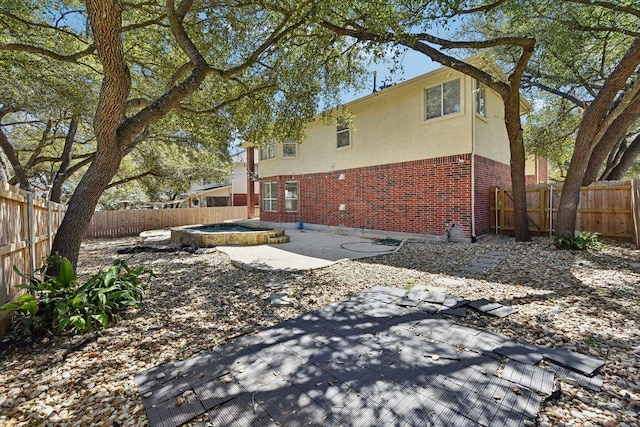 exterior space with a patio, an outdoor hot tub, a fenced backyard, and brick siding