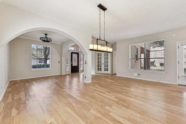 interior space with baseboards, arched walkways, and light wood finished floors