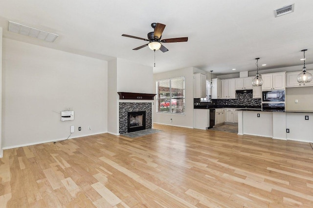 unfurnished living room with visible vents, a ceiling fan, light wood finished floors, baseboards, and a tile fireplace