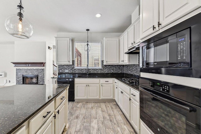 kitchen featuring tasteful backsplash, light wood-style flooring, hanging light fixtures, black appliances, and a sink