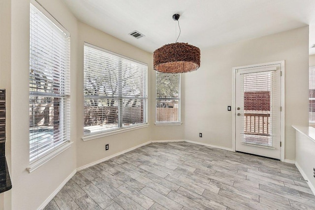 unfurnished dining area featuring wood finished floors, visible vents, a wealth of natural light, and baseboards