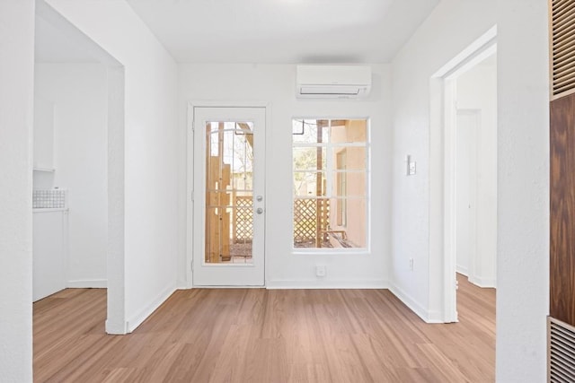 unfurnished room featuring baseboards, light wood-type flooring, and a wall mounted AC