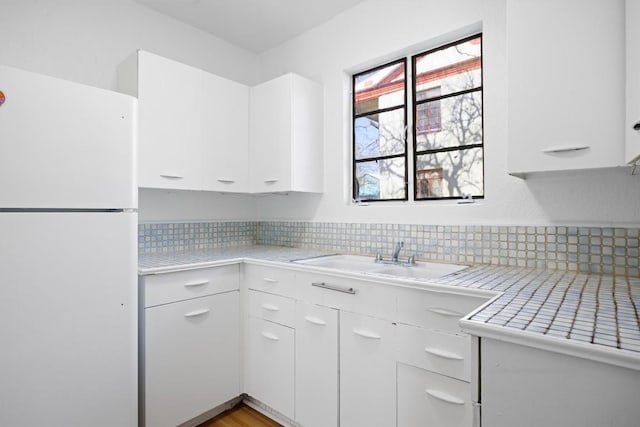 kitchen featuring a sink, white cabinetry, light countertops, and freestanding refrigerator