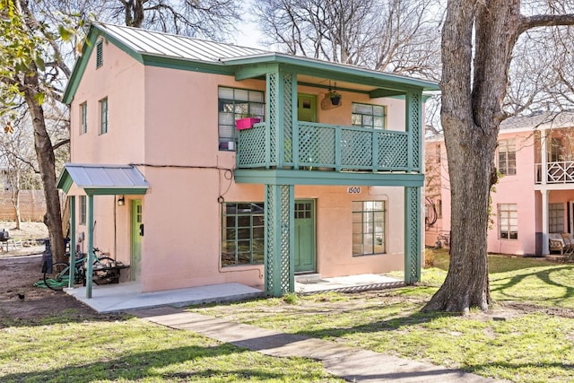 view of front facade with stucco siding, a front lawn, a standing seam roof, metal roof, and a balcony