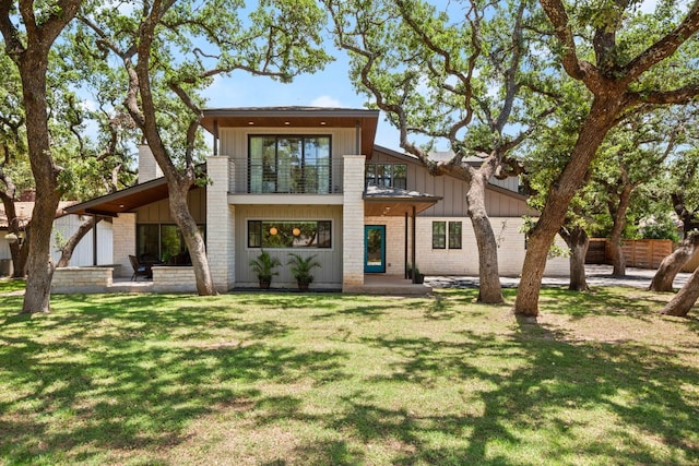 rear view of property featuring a lawn, a patio, a balcony, and board and batten siding