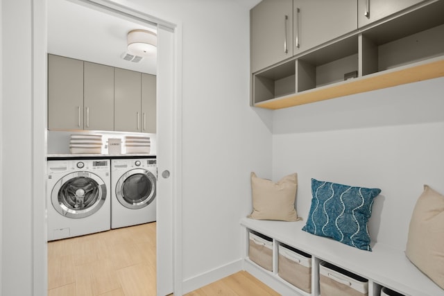 washroom with cabinet space, light wood-style flooring, washing machine and dryer, and visible vents