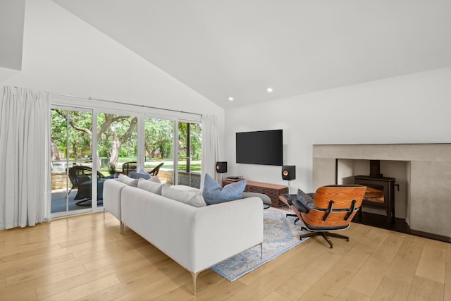 living room with recessed lighting, high vaulted ceiling, a wood stove, and light wood-style floors