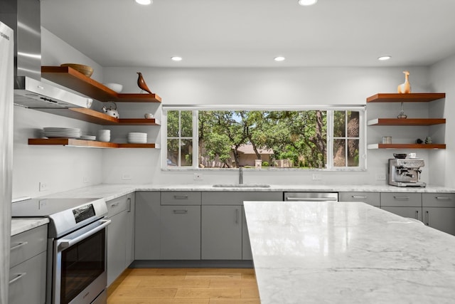 kitchen with open shelves, wall chimney exhaust hood, gray cabinets, and stainless steel appliances