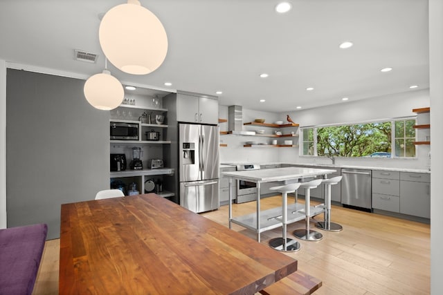 kitchen with visible vents, wall chimney range hood, gray cabinets, appliances with stainless steel finishes, and open shelves