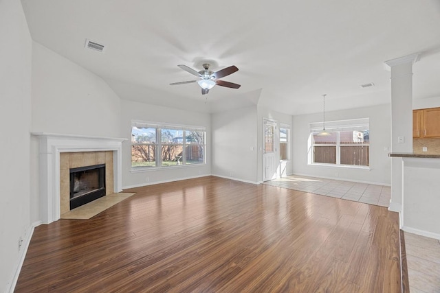 unfurnished living room with a ceiling fan, visible vents, decorative columns, a fireplace, and light wood-style floors