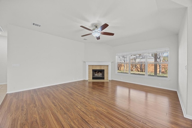 unfurnished living room featuring a tiled fireplace, visible vents, a ceiling fan, and wood finished floors