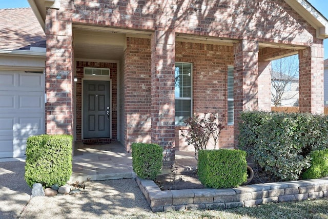 entrance to property featuring brick siding, roof with shingles, and an attached garage