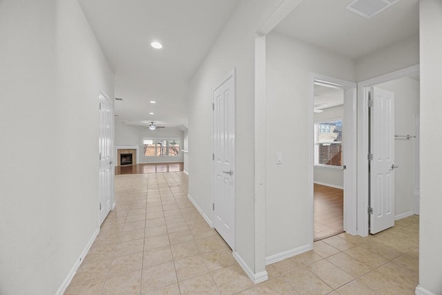 hallway featuring light tile patterned flooring, visible vents, plenty of natural light, and baseboards