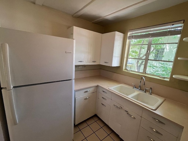 kitchen with light tile patterned floors, freestanding refrigerator, a sink, light countertops, and white cabinetry