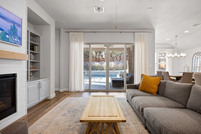 living room featuring light wood-style floors, a chandelier, a large fireplace, built in features, and healthy amount of natural light