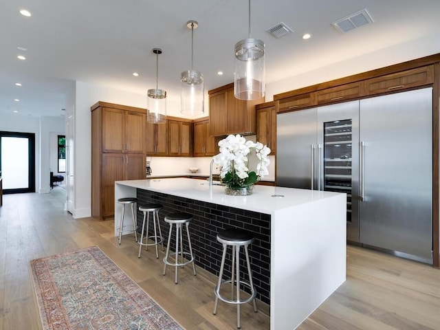 kitchen featuring visible vents, brown cabinets, built in refrigerator, and light wood-type flooring