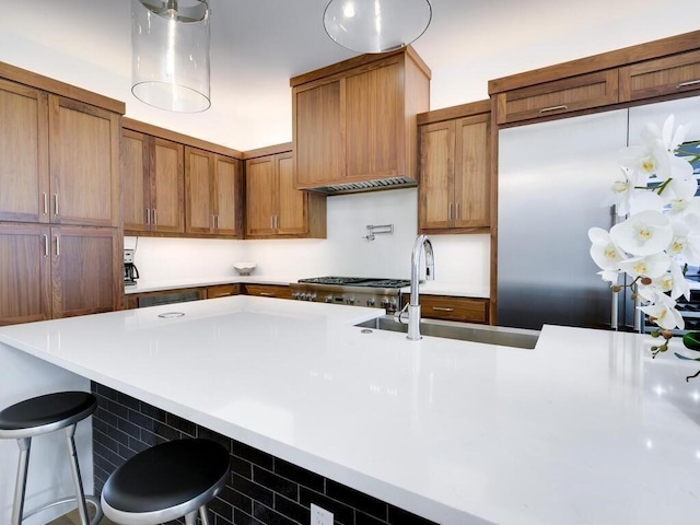 kitchen with a kitchen bar, a sink, brown cabinetry, light countertops, and stove