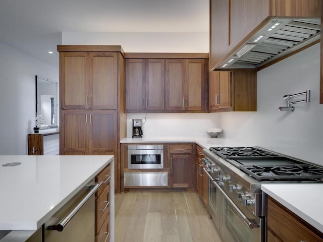 kitchen with brown cabinetry, light wood finished floors, range with two ovens, custom exhaust hood, and light countertops