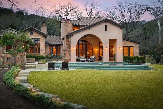 back of property at dusk with stone siding, a lawn, and a fenced in pool