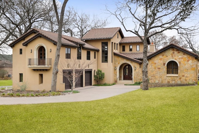 mediterranean / spanish-style house with a front yard, a balcony, stucco siding, a chimney, and concrete driveway