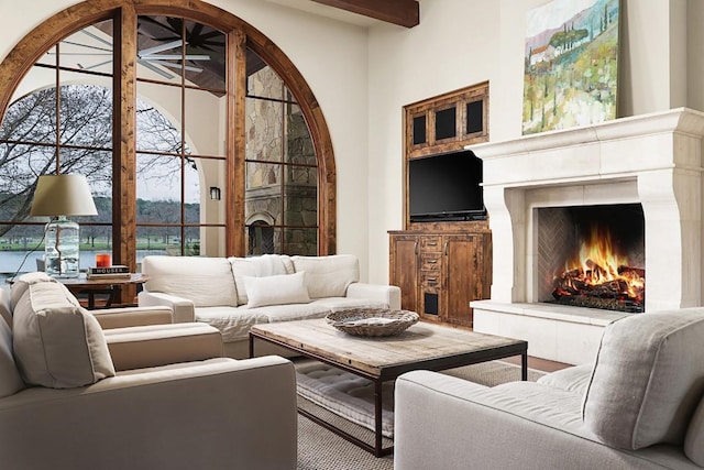 living room featuring beamed ceiling, a towering ceiling, and a lit fireplace