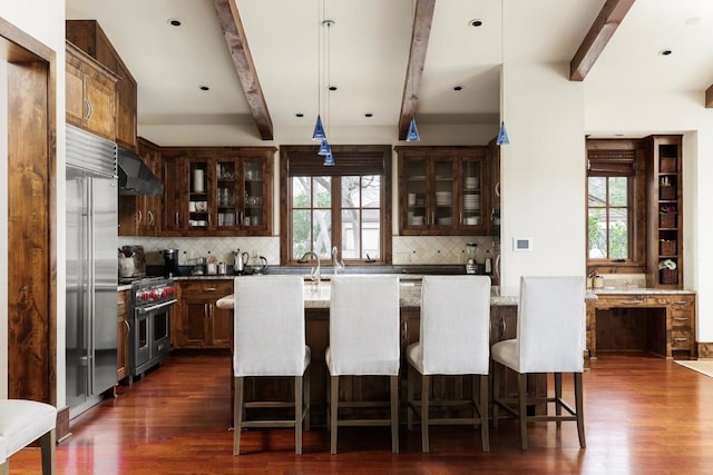 kitchen featuring range hood, high quality appliances, beamed ceiling, and a healthy amount of sunlight