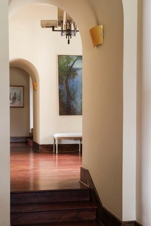 staircase featuring a chandelier, arched walkways, and wood finished floors