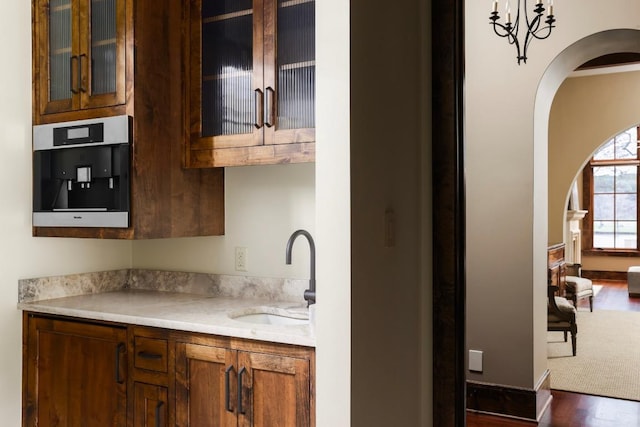 kitchen featuring glass insert cabinets, dark wood-type flooring, light countertops, brown cabinetry, and a sink