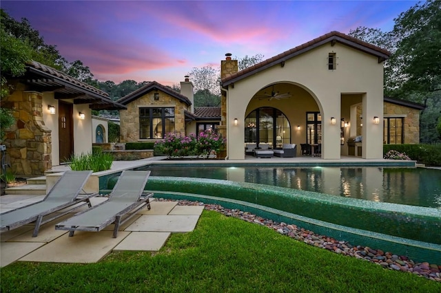 back of property featuring a chimney, a patio area, stone siding, and a ceiling fan