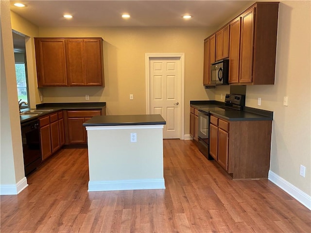 kitchen featuring a kitchen island, recessed lighting, black appliances, light wood-style floors, and dark countertops