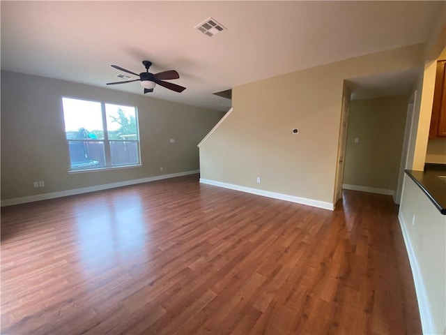 unfurnished living room with dark wood-style floors, baseboards, visible vents, and ceiling fan