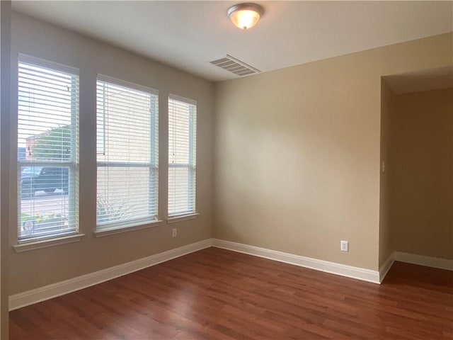 unfurnished room featuring visible vents, plenty of natural light, baseboards, and dark wood-style flooring