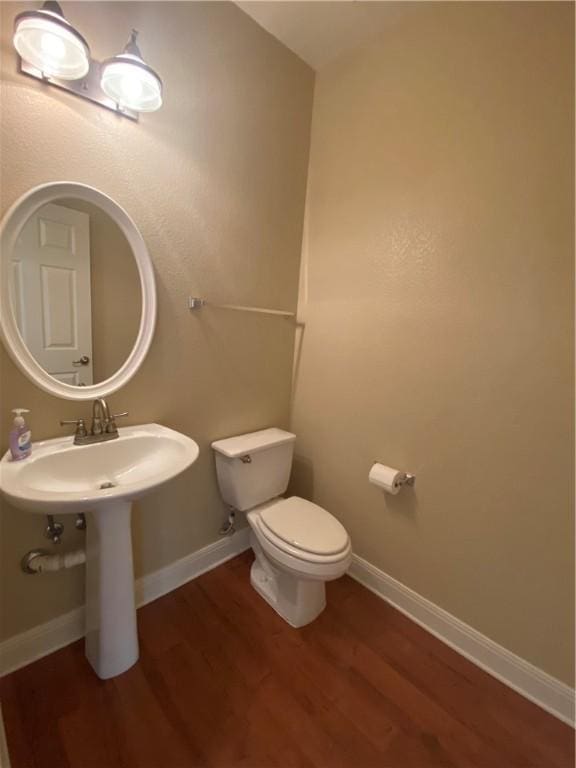 half bath featuring baseboards, toilet, and wood finished floors