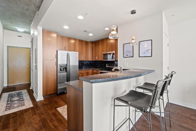 kitchen featuring dark wood-type flooring, decorative backsplash, a peninsula, brown cabinetry, and stainless steel appliances