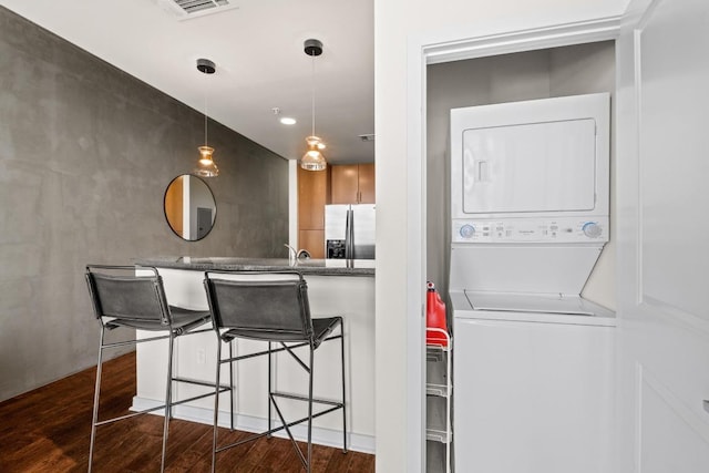 kitchen featuring visible vents, stainless steel fridge with ice dispenser, a kitchen bar, stacked washer and dryer, and dark wood-style flooring