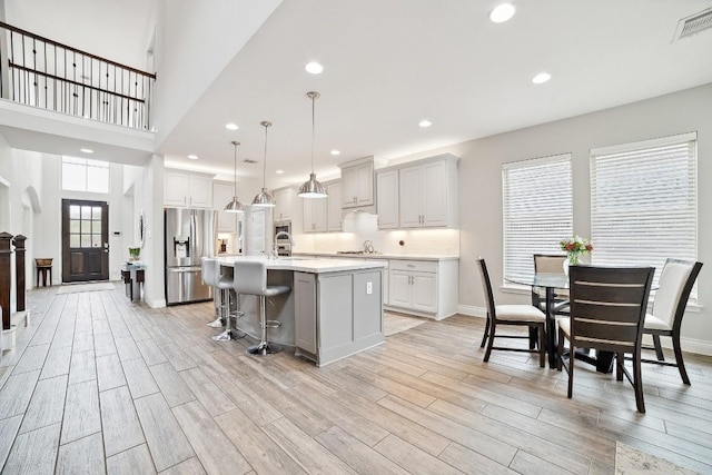 kitchen featuring wood finish floors, stainless steel fridge with ice dispenser, light countertops, recessed lighting, and a kitchen island with sink