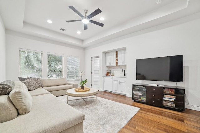 living area featuring visible vents, wood finished floors, indoor wet bar, a raised ceiling, and ceiling fan