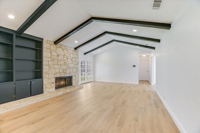 unfurnished living room featuring visible vents, lofted ceiling with beams, wood finished floors, a stone fireplace, and baseboards