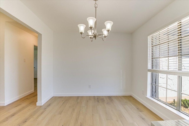 spare room featuring baseboards, a notable chandelier, and light wood finished floors