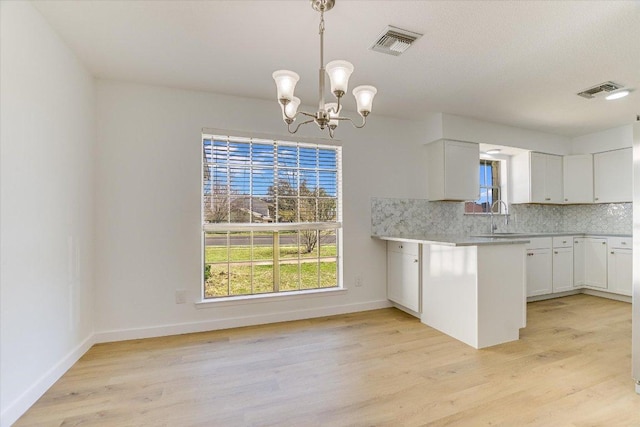 kitchen featuring visible vents, light wood finished floors, a sink, white cabinetry, and backsplash