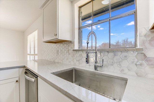 kitchen with stainless steel dishwasher, decorative backsplash, white cabinets, and a sink