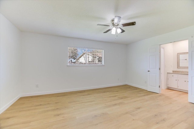 unfurnished bedroom featuring baseboards, ensuite bathroom, light wood-style floors, and a ceiling fan