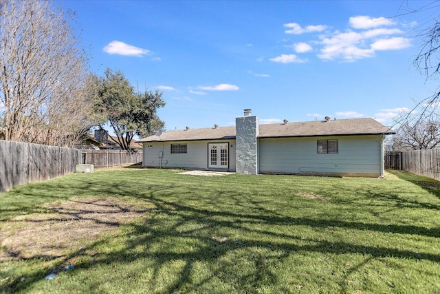 back of house featuring french doors, a lawn, a fenced backyard, and a chimney