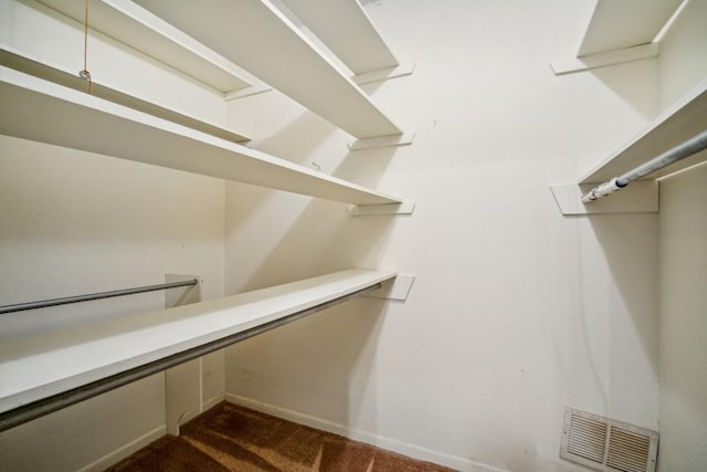 spacious closet featuring dark colored carpet and visible vents