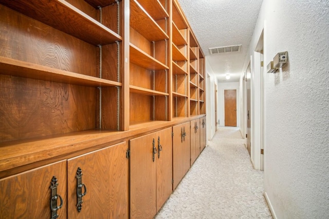 corridor featuring visible vents, light colored carpet, a textured ceiling, and a textured wall