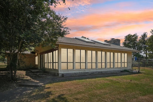 view of side of property with fence, a yard, a sunroom, a shingled roof, and a chimney