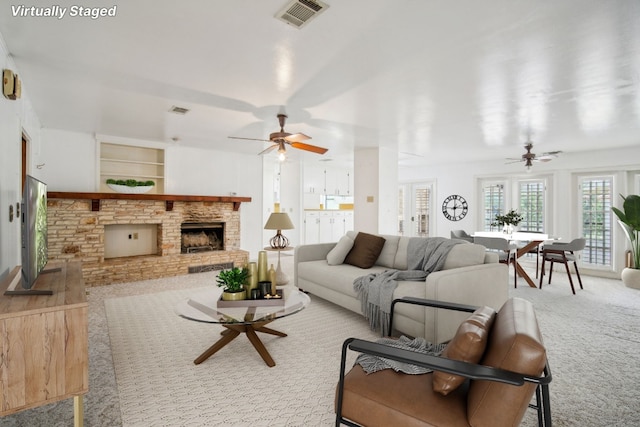 carpeted living room with visible vents, a fireplace with raised hearth, and a ceiling fan