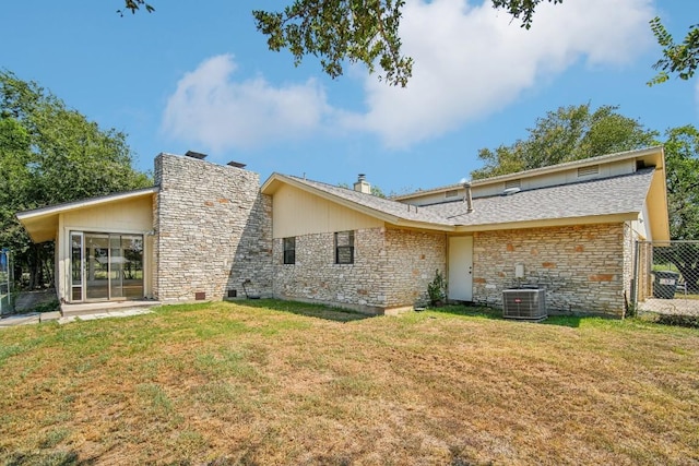 back of property with a yard, stone siding, central AC, and a chimney